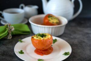 A stuffed tomato on a plate with breakfast crockery in the background