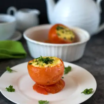 A stuffed tomato on a plate with breakfast crockery in the background