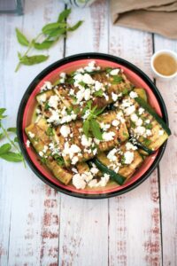 slices of grilled zucchini with crumbled feta cheese in a bowl.