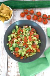 An overhead shot of a bowl of cucumber salsa with chopped tomatoes