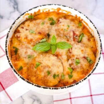 Cheesy eggplant casserole topped with crispy Parmesan in a white bowl with basil leaves.