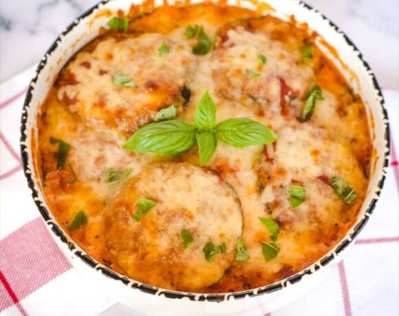 Cheesy eggplant casserole topped with crispy Parmesan in a white bowl with basil leaves.