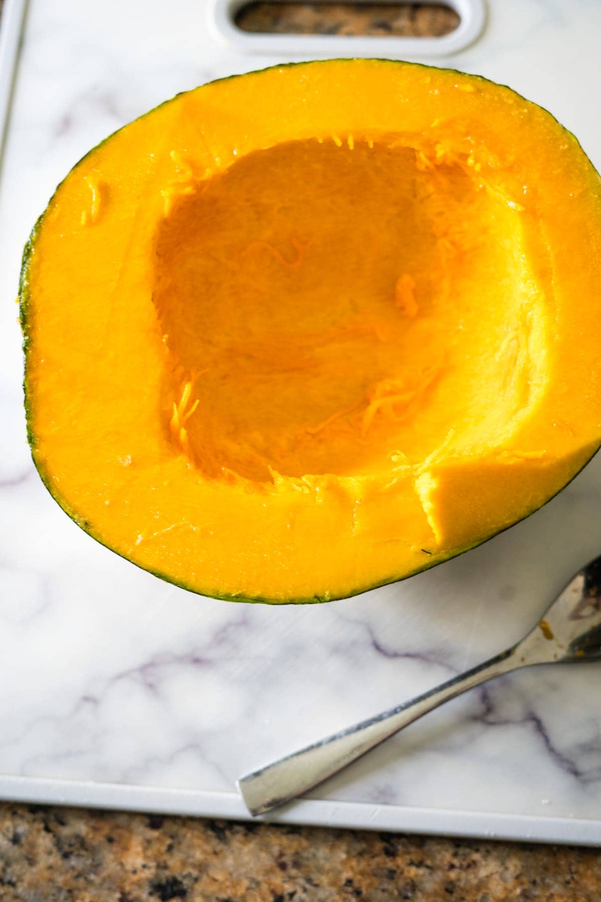 A pumpkin is cut in half and sitting on a cutting board, ready to be transformed into delectable pumpkin fries.