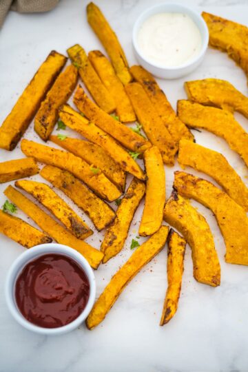 A plate of pumpkin fries with ketchup and dipping sauce.