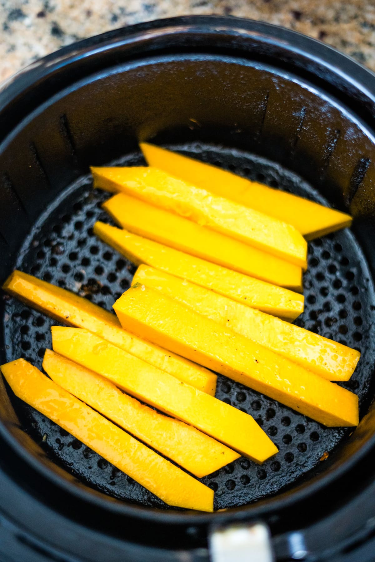 An air fryer filled with sliced pumpkin fries.