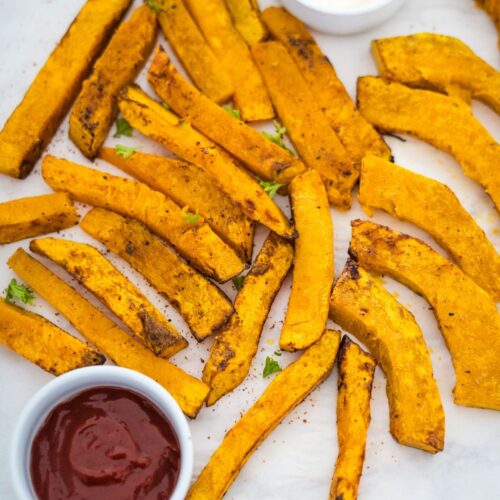 A plate of sweet potato pumpkin fries with ketchup and dipping sauce.