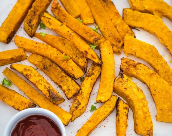 A plate of sweet potato pumpkin fries with ketchup and dipping sauce.