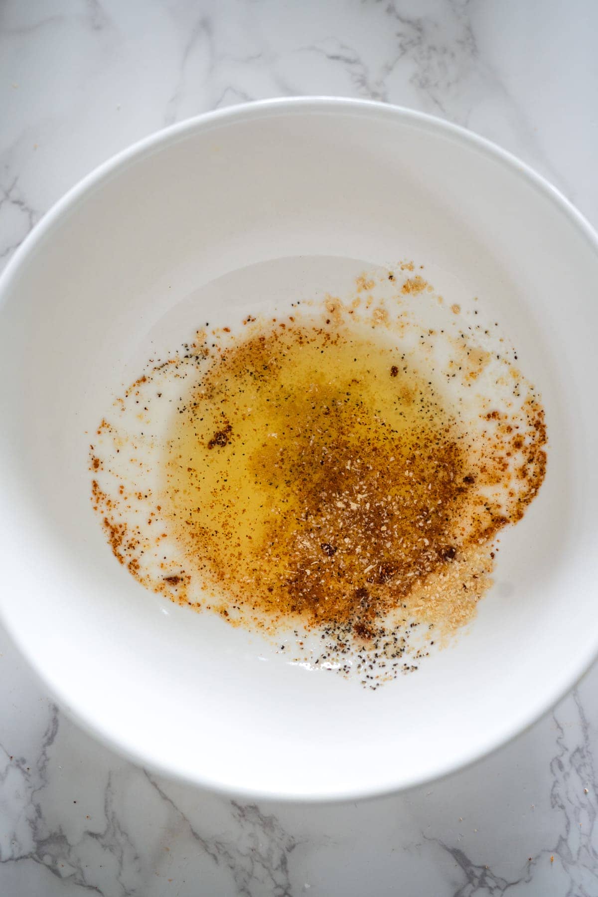 A white bowl filled with a mixture of pumpkin fries, oil, and spices.