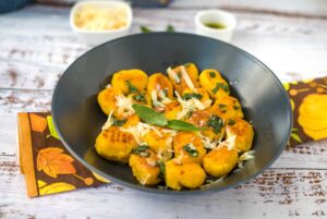 Pumpkin gnocchi with sage leaves and grated cheese in a grey bowl.