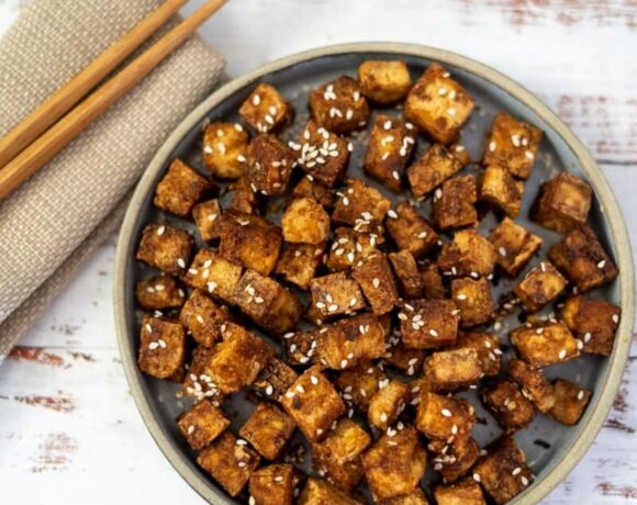 Crispy tofu in a bowl with chopsticks and sesame seeds, made in an air fryer.