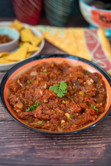 A bowl of chipotle-infused mexican chili with tortilla chips on a wooden table.