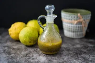 A bottle of keto poppy seed dressing next to a bowl of lemons.
