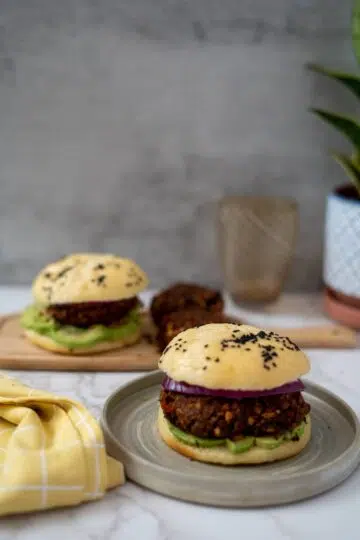 Two black bean burgers on a plate next to a plant.