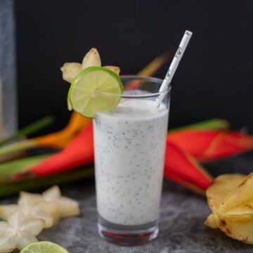 star fruit smoothie in a tall glass with a straw and sliced lime on the rim