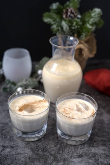 Two glasses of vegan coquito in front of a pitcher.