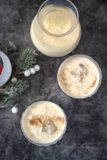Three glasses of vegan coquito with cinnamon and icing on a table.