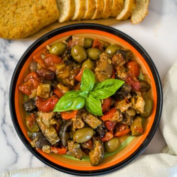vegetable caponata in a bright circular plate, topped with fresh basil