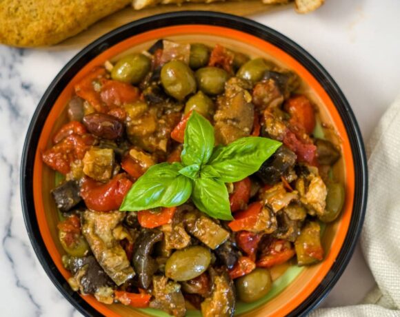 vegetable caponata in a bright circular plate, topped with fresh basil