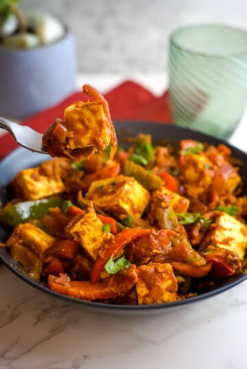 a fork lifting a piece of paneer jalfrezi from a bowl