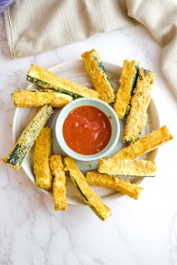 air fryer zucchini fries on a circular plate with a dip in the middle