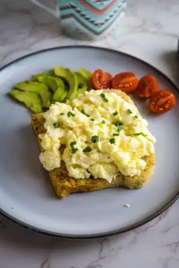 A plate with scrambled eggs, avocado, tomatoes and a cup of coffee. Keywords: scrambled eggs.