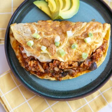 An omelet with meat and avocado on a plate.