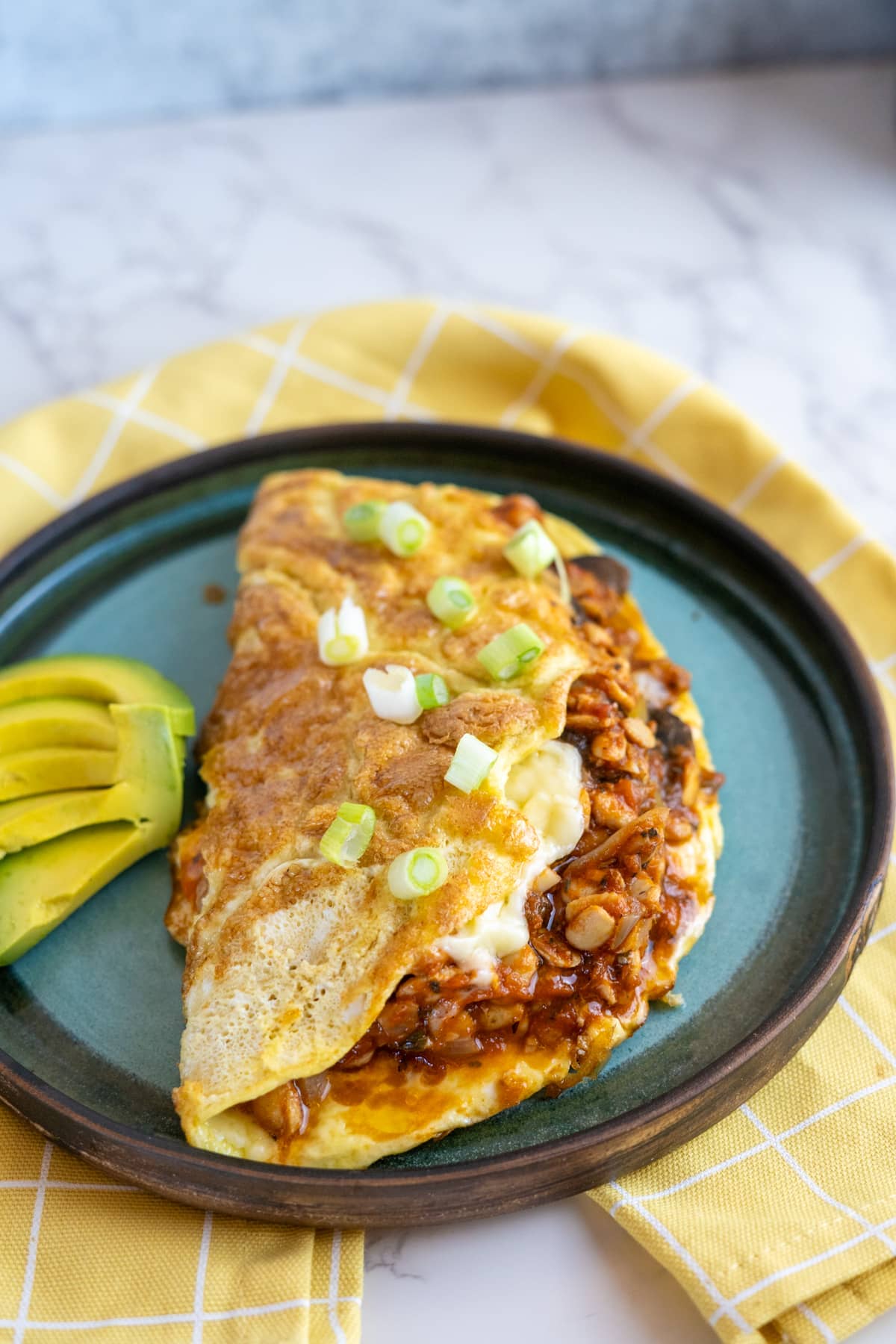 A plate with an omelet and avocado on it.