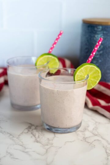 Two glasses of cottage cheese smoothie with lime slices and straws.