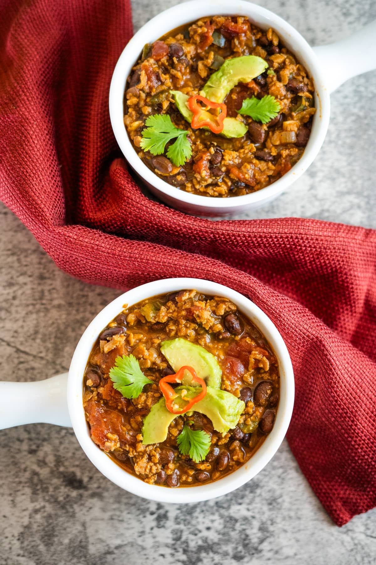 Two bowls of black bean chili with TVP on a red cloth.