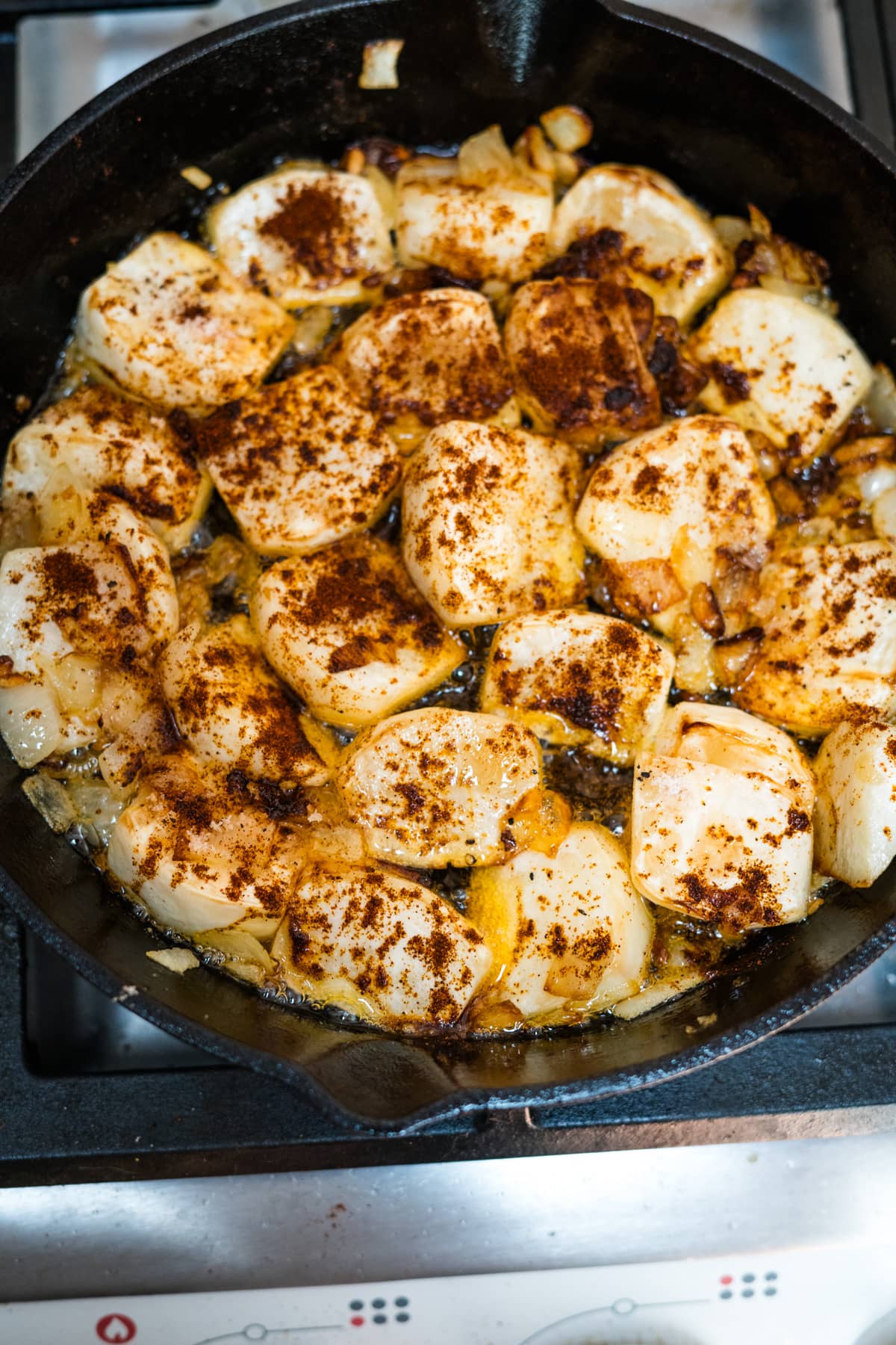 A skillet full of fried turnips on a stove top.