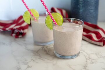 Two glasses of cottage cheese smoothie with lime slices and straws.