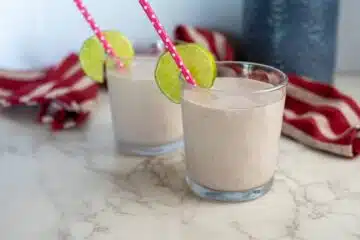 Two glasses of cottage cheese smoothie with lime slices and straws.