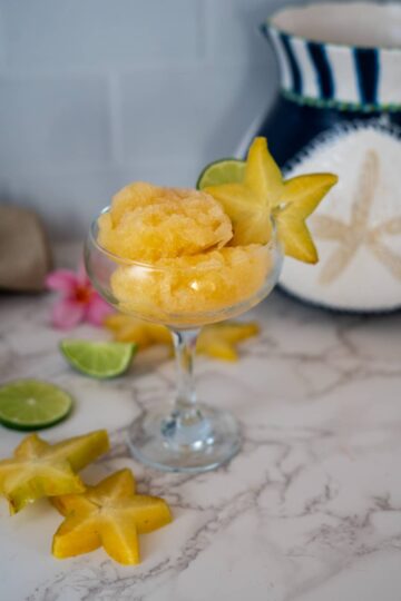Mango ice cream in a glass with lime and star shaped garnishes featuring star fruit sorbet.