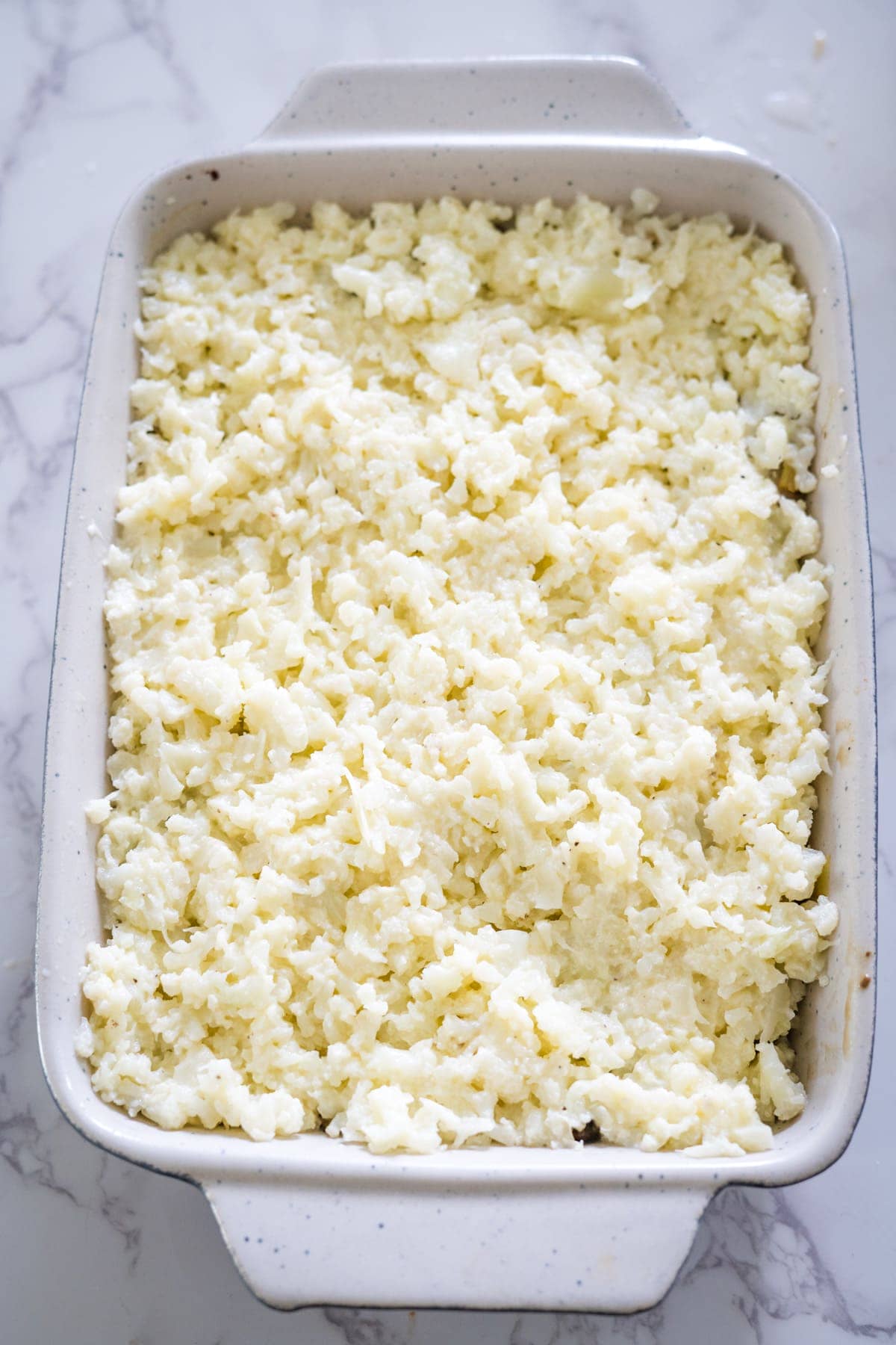 A delectable mushroom and leek cottage pie served in a white baking dish, topped with a generous layer of melted shredded cheese.