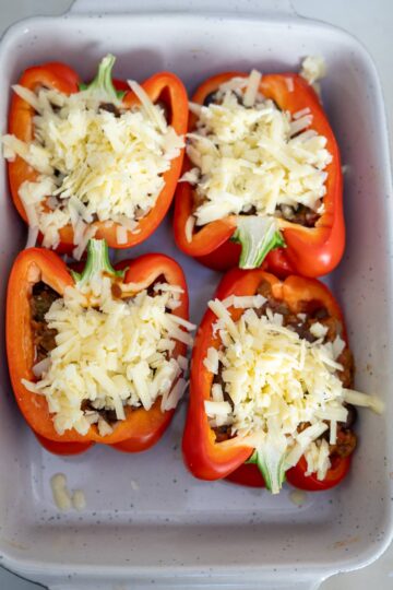 Stuffed peppers with meat and cheese in a baking dish.