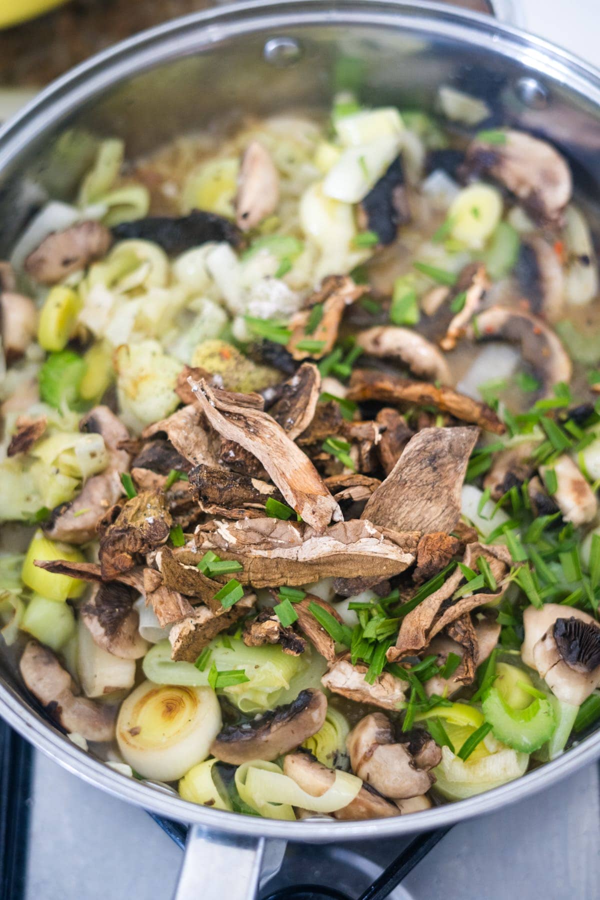 A pan full of mushrooms and vegetables simmering on a stove, preparing for a mouthwatering mushroom and leek cottage pie.