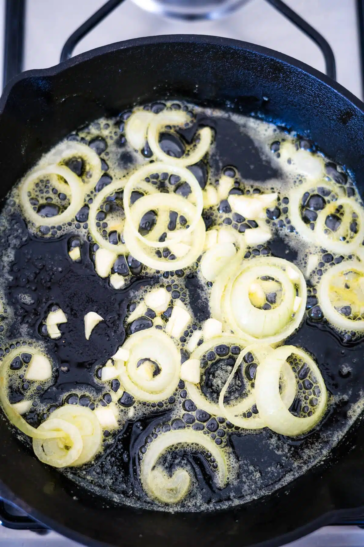 A frying pan with onions, zucchini, and mushrooms in it.