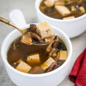 Tofu and mushroom soup in a bowl with a spoon.