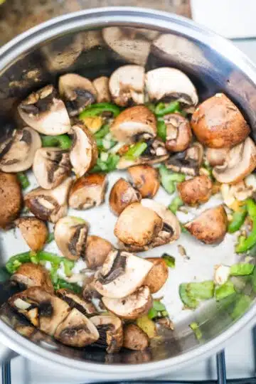 Cooking mushrooms in a pan on a stove top to prepare mushroom tofu soup.