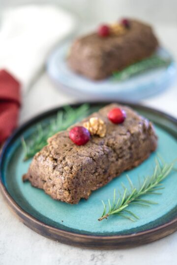 A cake with cranberries and sprigs of rosemary on a plate.