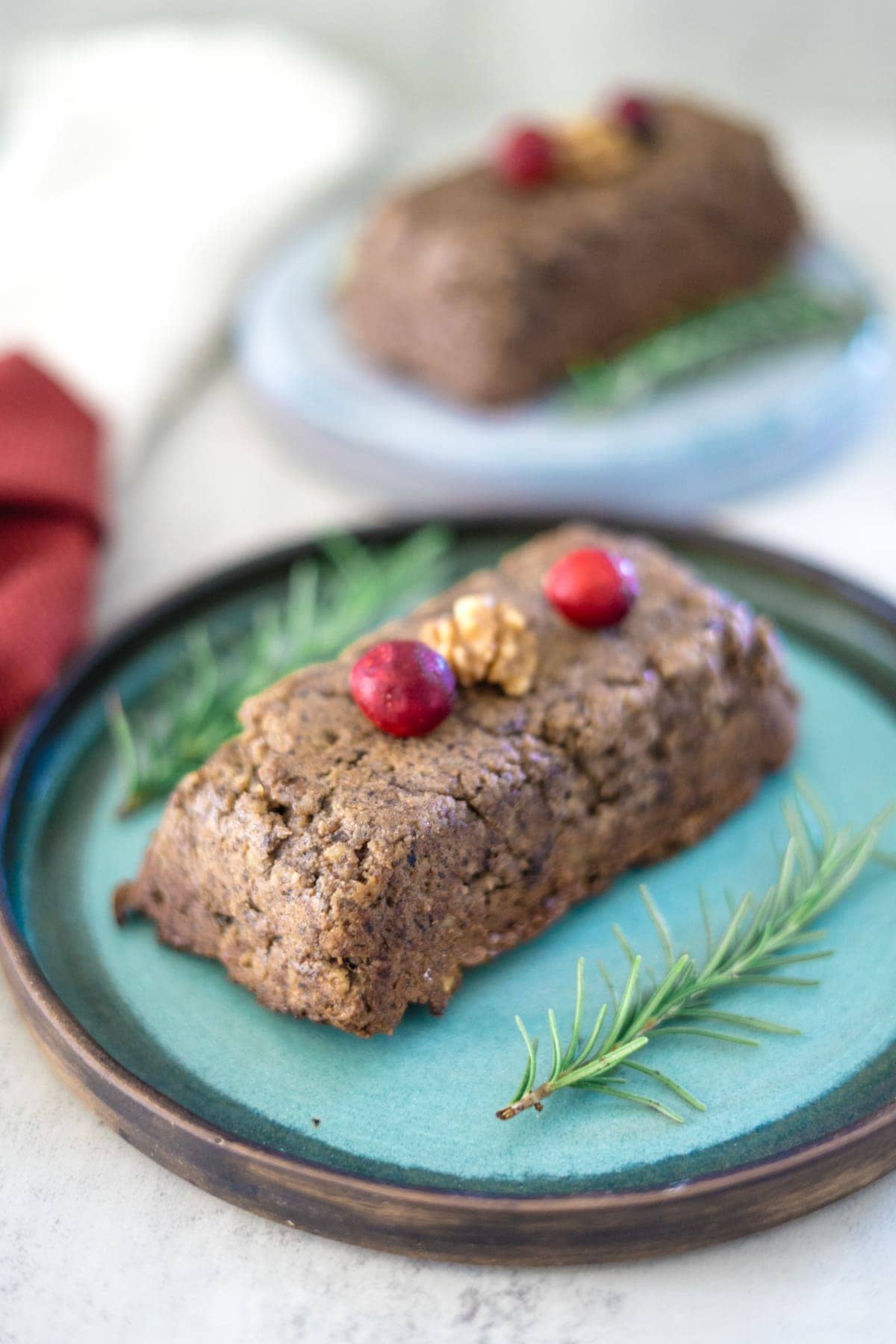 A cake with cranberries and sprigs of rosemary on a plate.