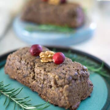 A cake with cranberries and sprigs of rosemary on a plate.