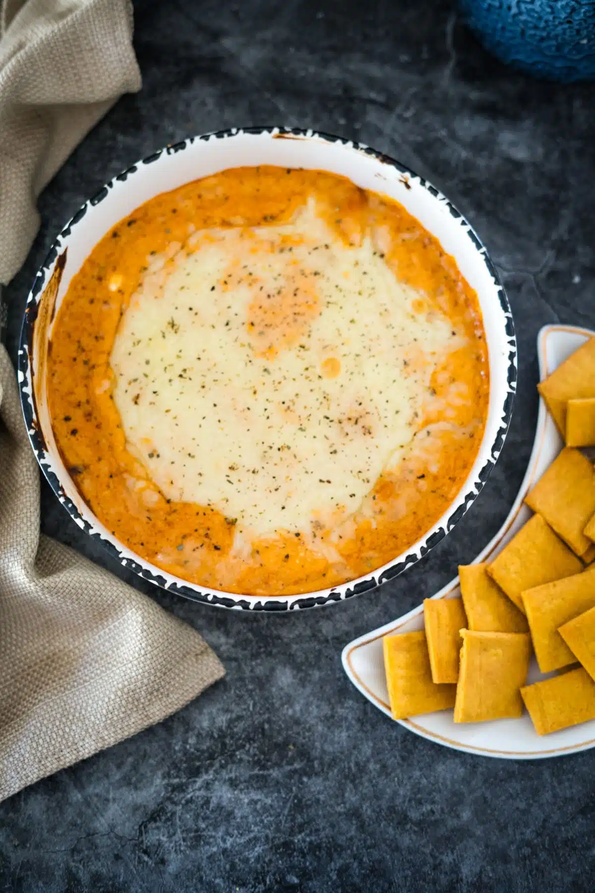 A bowl of cheesy dip with crackers next to it.