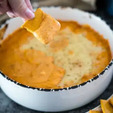 A person dipping a cracker into a bowl of cheese dip.