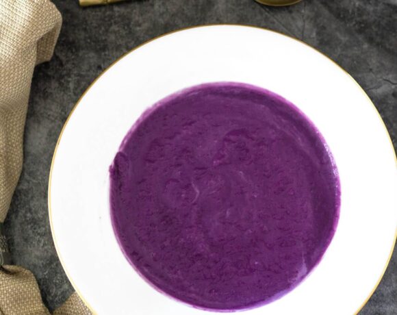 A bowl of purple soup with a spoon next to it.