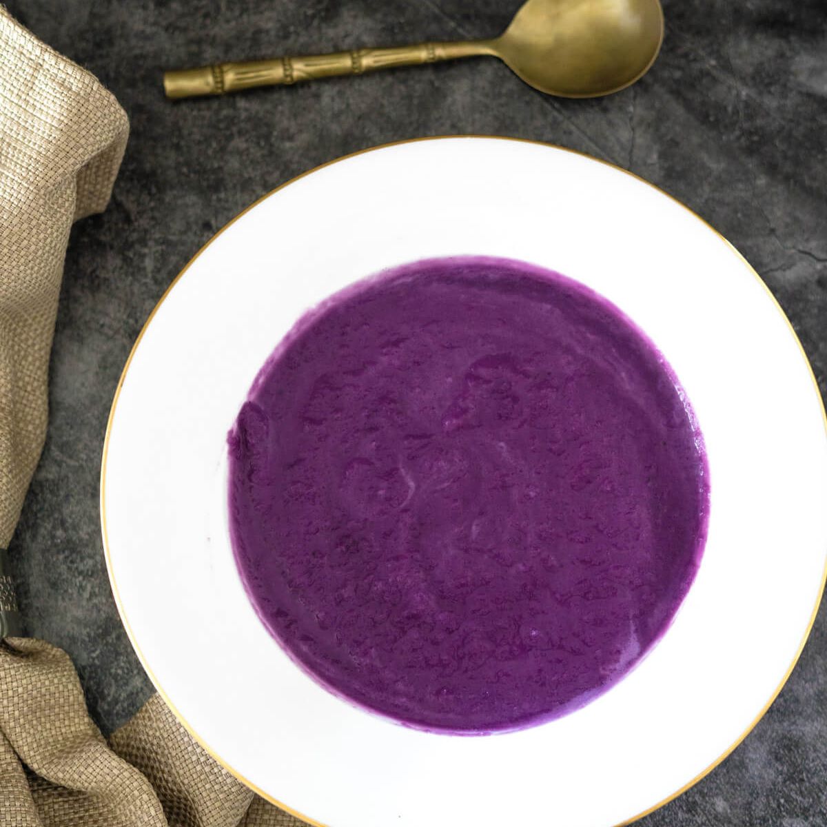 A bowl of purple soup with a spoon next to it.