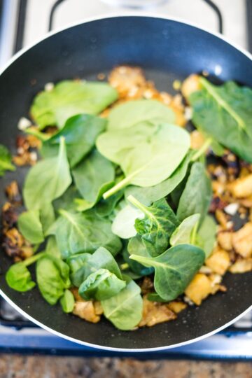 Eggplant boats with spinach cooked in a frying pan on a stove.