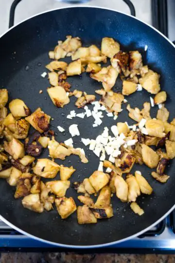 A frying pan on a stove top, cooking delicious eggplant boats.