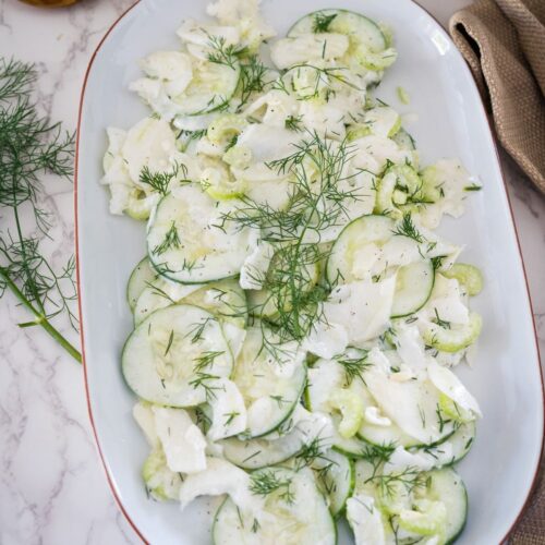 A white plate with cucumbers and dill on it.