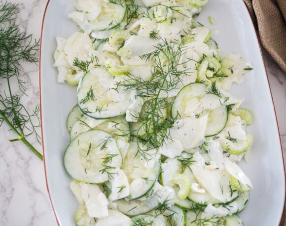 A white plate with cucumbers and dill on it.